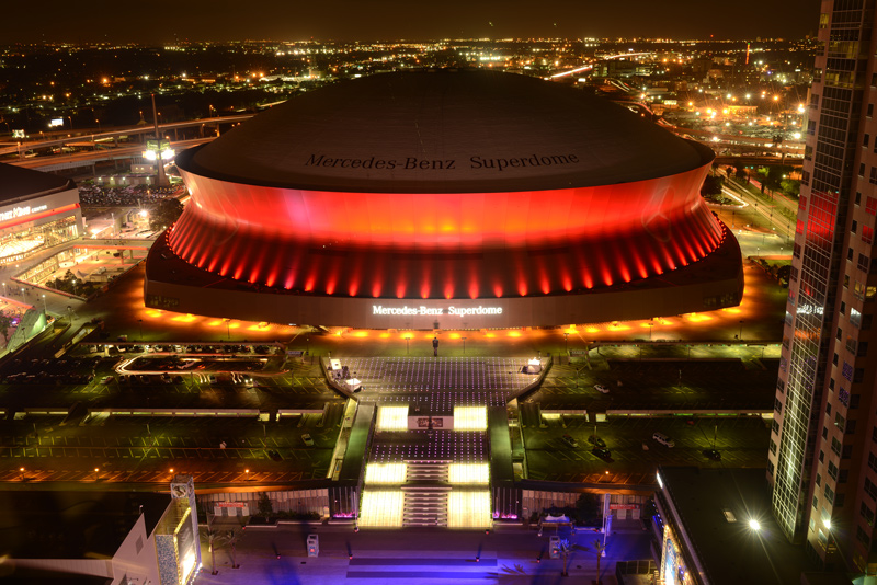 Football Caesars Superdome at night, lit up with red lights.
