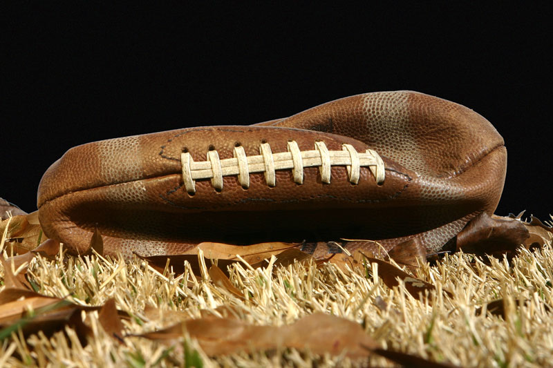 Deflated football lying in dead grass.