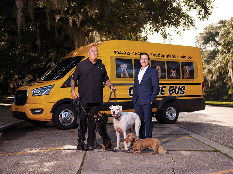 Rideshare Troy Bergeron (holding the leashes of three dogs) and Mario DeLuca standing outside in front of the Doggie Bus