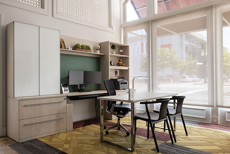 KV Workspace Interior, office has a clear, close view of the WWII Museum just across the street. Office features a clean table with a swivel chair facing two modern chairs. Behind the swivel chair is a dual monitor set up.
