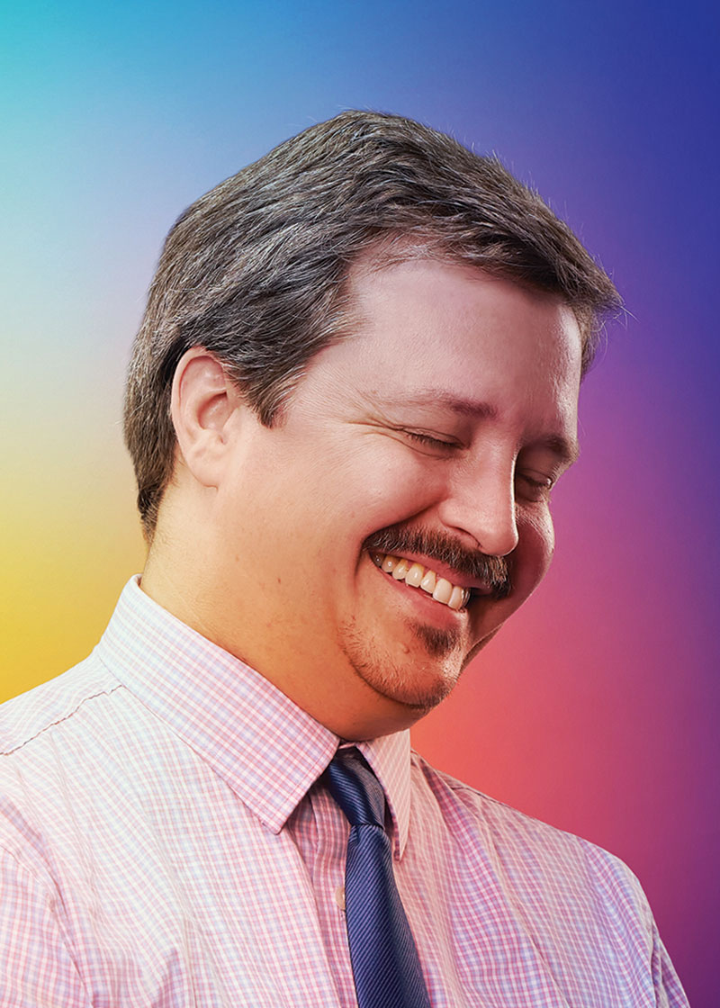 Another chest up photo of Knudsen. His face is angled to his left and his eyes are closed. He is mid light laugh.