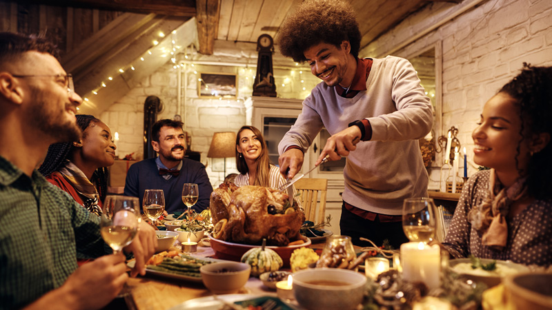 Group of adults celebrating Thanksgiving and passing around food around a set table.