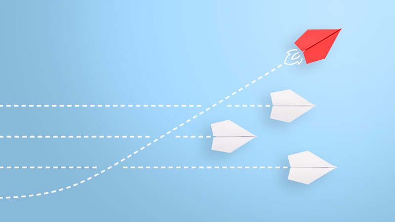 Four paper airplanes flying against a blue background, with dotted lines behind to indicate motion. There is one airplane in particular that is angled more upwards than the other three (it is red-colored)