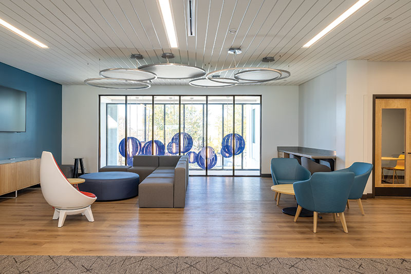 Dillard University Open big room featuring tall windows, a big sectional couch, a long counter in the corner, and comfortable blue chairs. In the back right there are more private work rooms.
