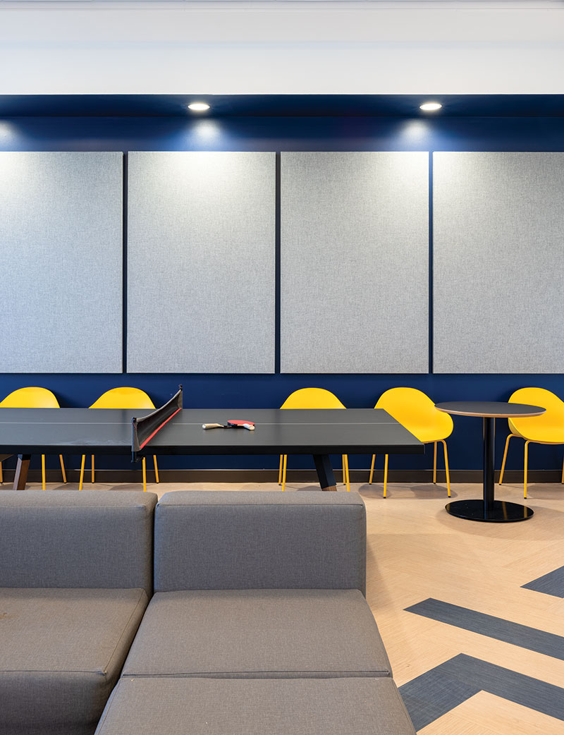 Another sectional; behind it is a table for table tennis and yellow chairs.